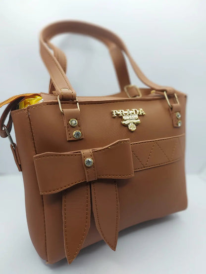 Luxurious camel brown tote bag with a silk-textured finish, bow charm accent, gold-tone Prada-inspired logo, and dual carrying options for versatile styling