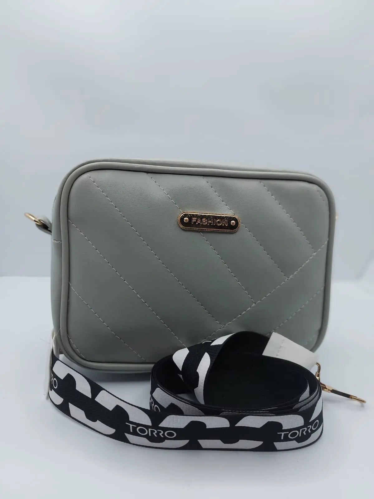 Chic light grey quilted crossbody bag with a gold-tone logo plate and a trendy adjustable strap for a modern everyday look.